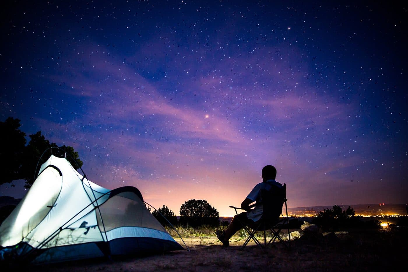 A camper in a chair beside a tent under a starry night sky